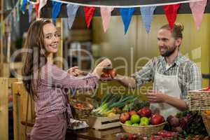 Smiling vendor giving tomatoes to woman at the counter in the grocery store