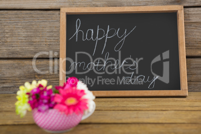 Happy mothers day text written on chalk board with cup of flowers