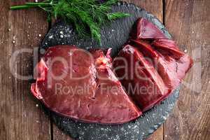 Raw liver on slate board on wooden background top view