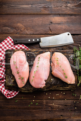 Raw chicken breasts fillets with thyme and spices on wooden cutting board on rustic background copy space directly above