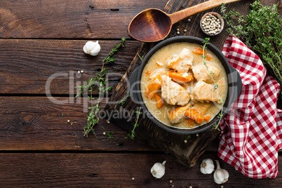 Meat stewed with carrots in sauce and spices in cast iron pan on dark wooden rustic background top view flat lay