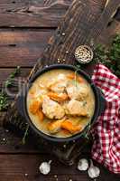 Meat stewed with carrots in sauce and spices in cast iron pan on dark wooden rustic background top view flat lay