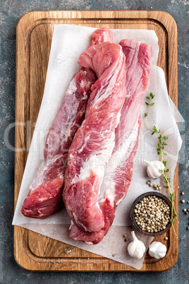 Fresh raw pork tenderloin on wooden cutting board on dark background