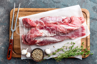 Fresh raw pork tenderloin on wooden cutting board on dark background