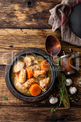 Meat stewed with carrots in sauce and spices in cast iron pot on dark wooden rustic background