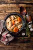 Meat stewed with carrots in sauce and spices in cast iron pot on dark wooden rustic background