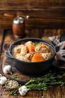 Meat stewed with carrots in sauce and spices in cast iron pot on dark wooden rustic background