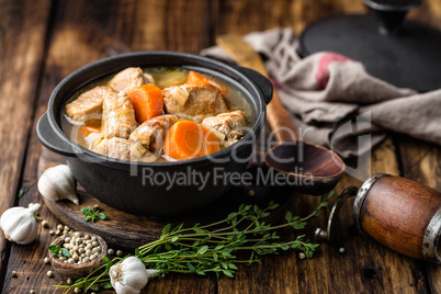 Meat stewed with carrots in sauce and spices in cast iron pot on dark wooden rustic background