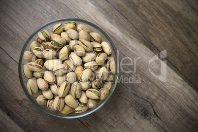 Glass bowl of pistachios on wooden background