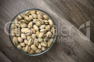 Glass bowl of pistachios on wooden background