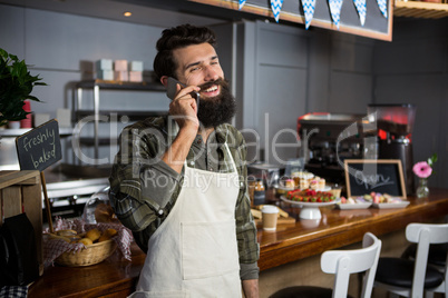 Smiling male staff talking on mobile phone at counter in coffee shop