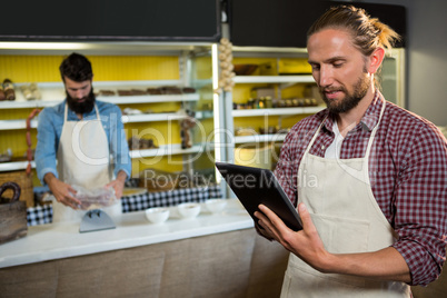 Male staff using digital tablet near meat counter