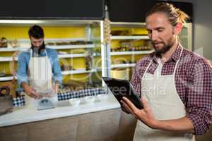 Male staff using digital tablet near meat counter