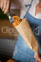 Mid-section of female staff packing sweet food in paper bag
