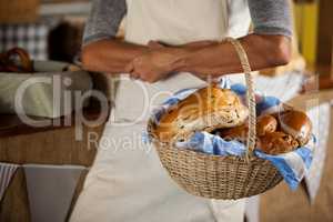 Mid-section of female staff holding wicker basket of breads at counter
