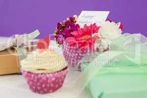 Cup cake, gift box and fresh flowers on wooden surface