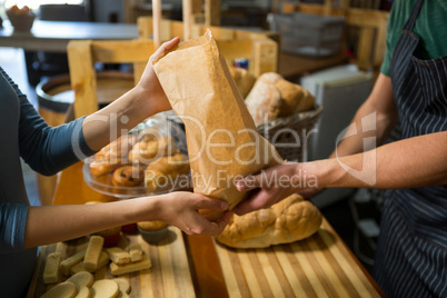 Smiling female customer receiving a parcel from bakery staff at counter