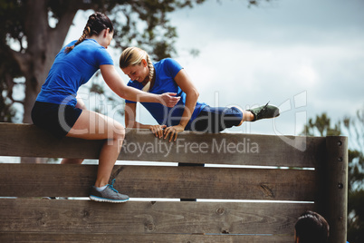 Female trainer assisting woman to climb a wooden wall