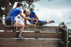 Female trainer assisting woman to climb a wooden wall