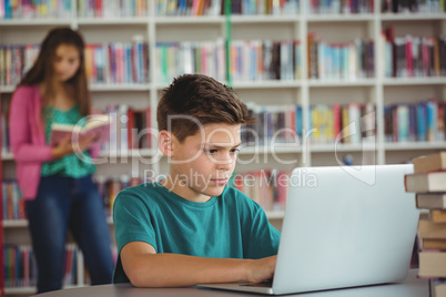 Schoolboy using laptop in library at school