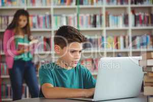 Schoolboy using laptop in library at school