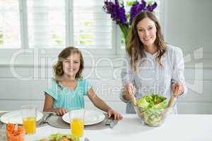 Portrait of smiling mother and daughter mixing bowl of salad in kitchen
