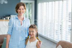 Portrait of smiling mother and daughter standing together in living room