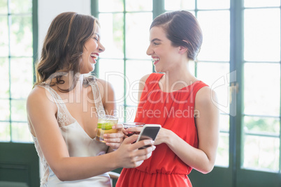 Friends with cocktail glasses laughing while using mobile phone