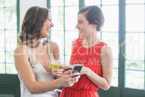 Friends with cocktail glasses laughing while using mobile phone