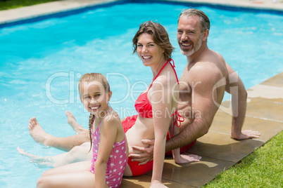 Portrait of parents and daughter sitting on poolside in pool water