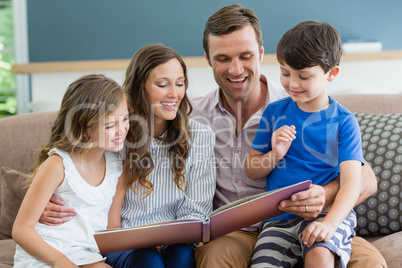 Family sitting on couch looking at photo album in living room at home