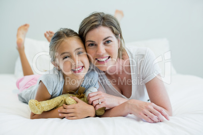 Portrait of smiling mother and daughter lying on bed in bedroom