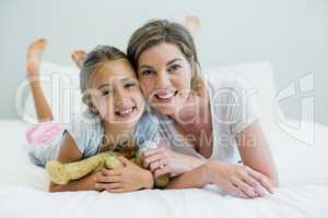 Portrait of smiling mother and daughter lying on bed in bedroom