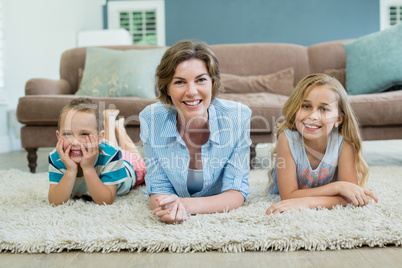 Smiling mother with her son and daughter lying on carpet in living room