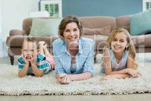 Smiling mother with her son and daughter lying on carpet in living room