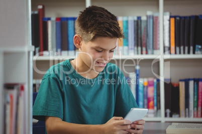 Smiling schoolboy using mobile phone in library