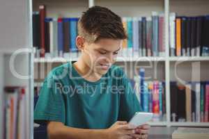 Smiling schoolboy using mobile phone in library