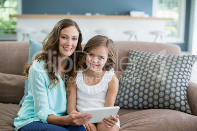 Smiling mother and daughter sitting on sofa using laptop in living room at home