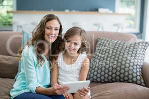 Smiling mother and daughter sitting on sofa using laptop in living room at home