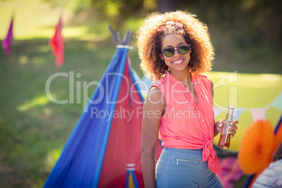 Portrait of woman holding beer bottle standing at campsite