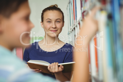 Smiling schoolgirl reading book in library at school