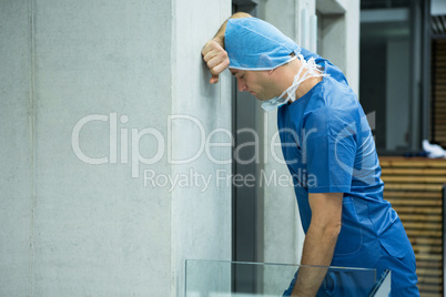 Tensed male surgeon leaning on wall near elevator