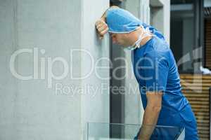 Tensed male surgeon leaning on wall near elevator