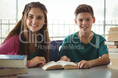 Smiling school kids reading books in library at school