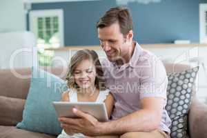 Smiling father and daughter sitting on sofa using digital tablet in living room