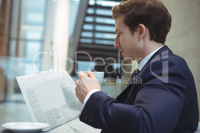 Businessman reading newspaper while having coffee