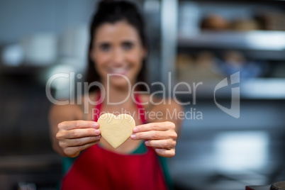 Close-up of female staff showing heart shape cookie at counter