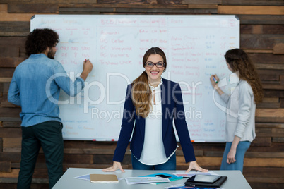 Portrait of smiling Businesswoman leaning on table while colleague working in background