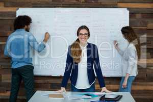 Portrait of smiling Businesswoman leaning on table while colleague working in background