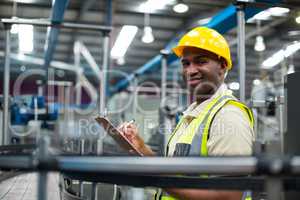 Portrait of smiling factory worker writing on clipboard in factory
